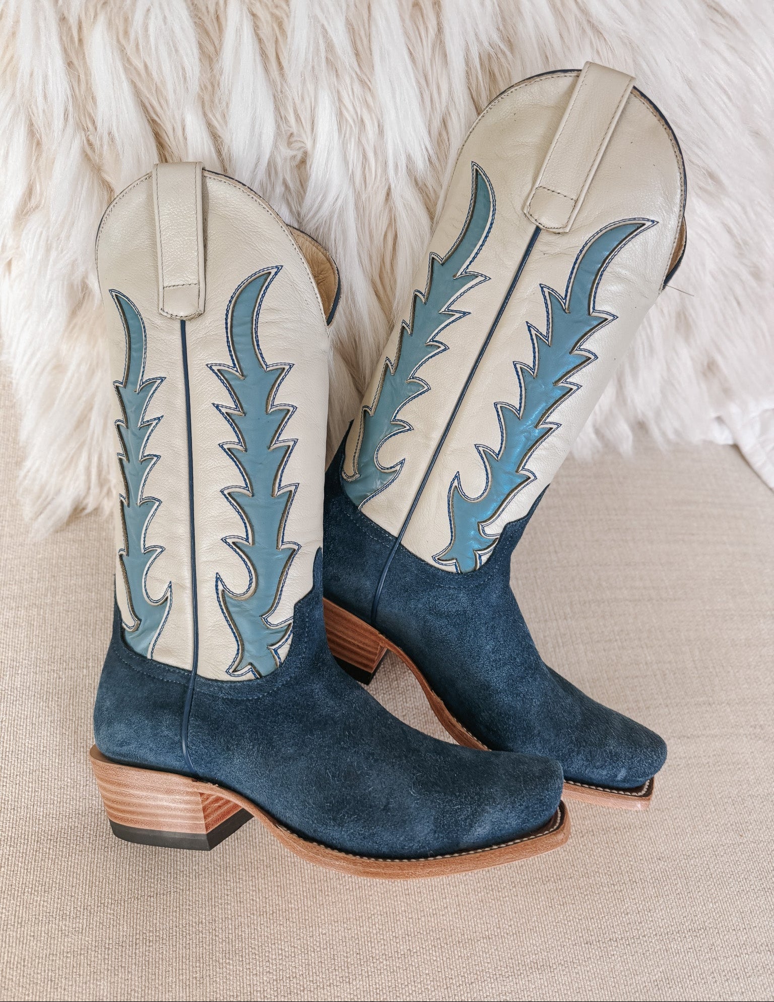 Blue and beige cowboy boots with decorative patterns on a textured surface